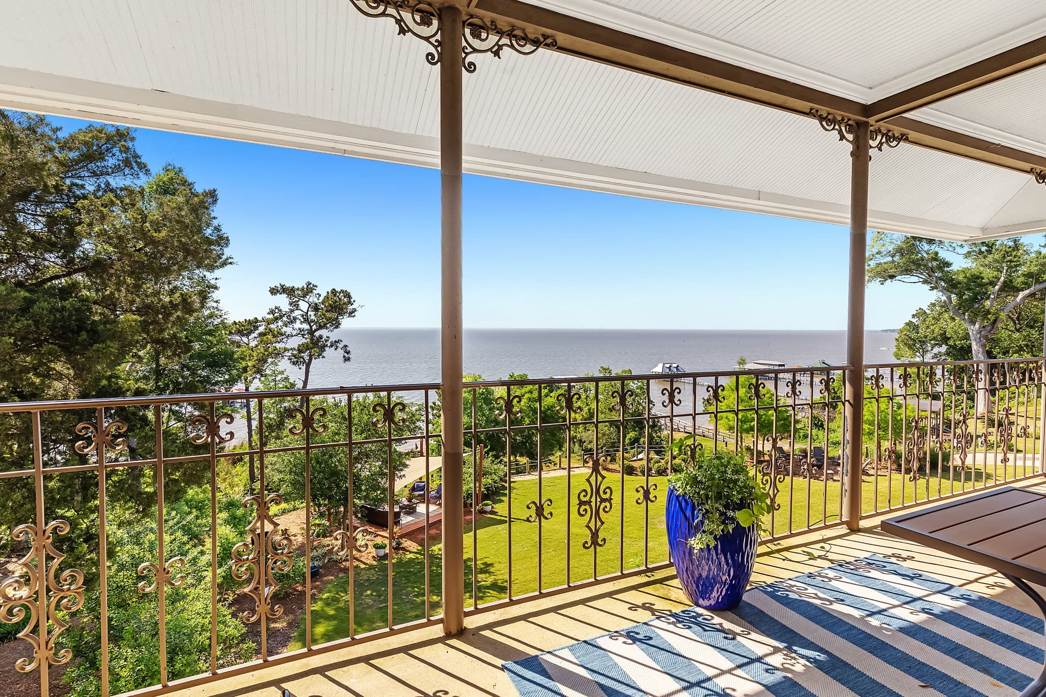 A balcony with ornate railings overlooking a serene waterfront and lush greenery.