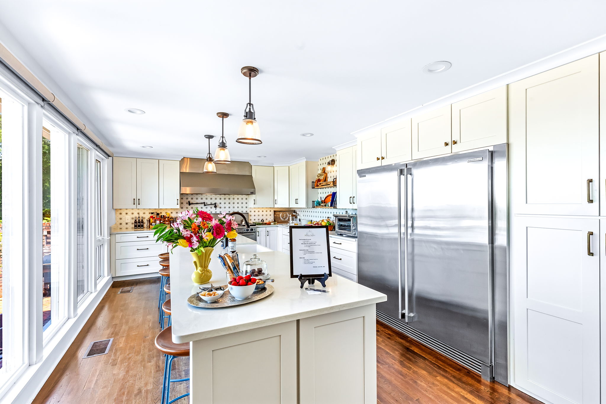 A spacious kitchen featuring white cabinets, stainless steel appliances, a large kitchen island with bar stools, and a variety of colorful accents.