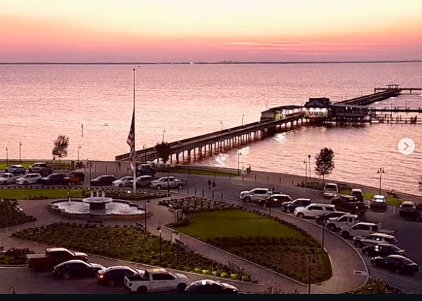A serene waterfront scene at sunset, featuring a pier and nearby vehicles.