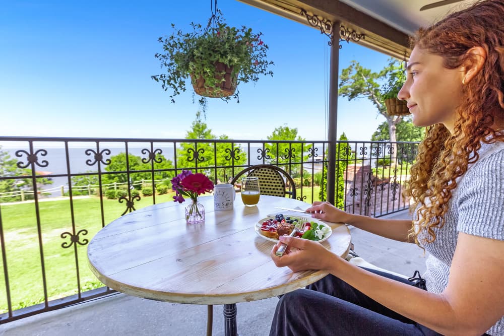 A woman sitting out on a veranda with a wrought iron fence, eating breakfast, looking out over the beautiful waters of Mobile Bay.