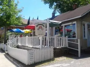 A cozy restaurant with a white picket fence, colorful umbrellas, and outdoor seating on a sunny day.