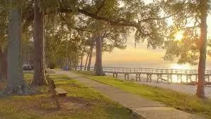 A peaceful waterfront scene with a walkway lined by trees and a dock at sunset.