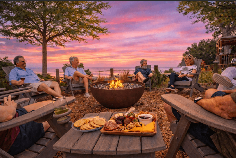A cozy gathering around a fire pit at sunset, with friends enjoying snacks and drinks.