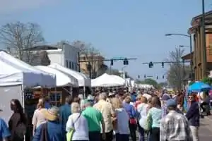 A crowded outdoor market with white tents lining the street under a clear blue sky.