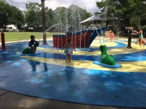 Children playing in a colorful splash pad with water features on a sunny day.
