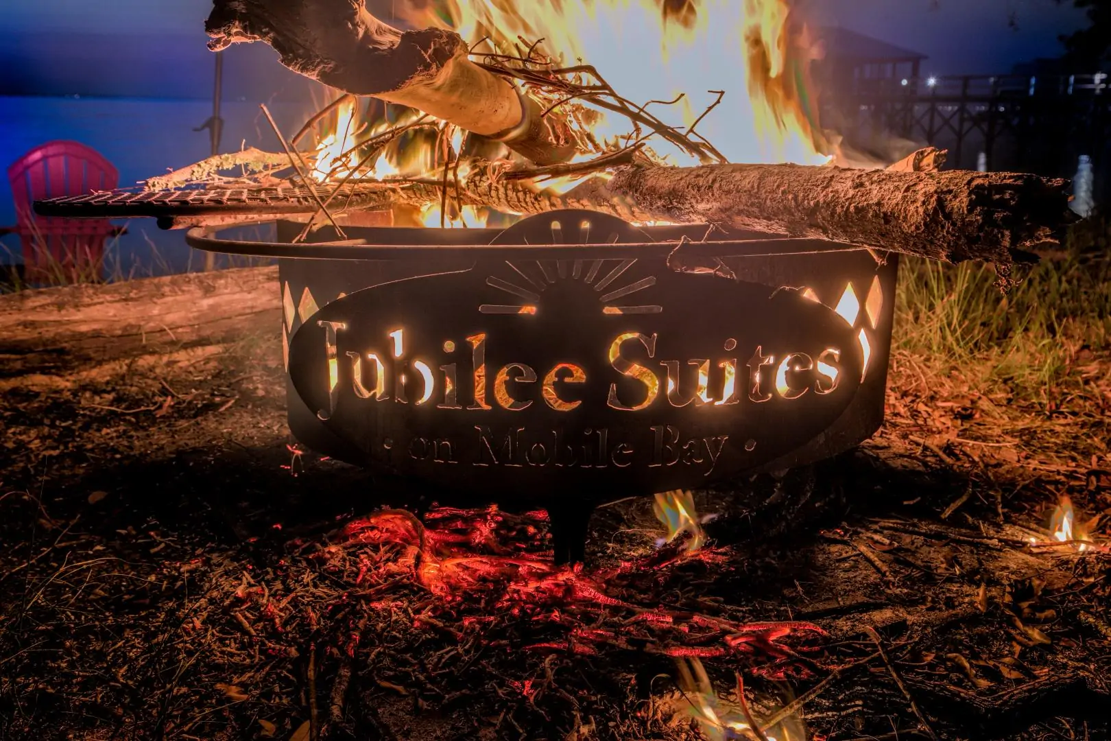 A glowing fire pit with the inscription "Jubilee Suites on Mobile Bay" surrounded by flames and logs. A glowing fire pit with the inscription "Jubilee Suites on Mobile Bay" surrounded by flames and logs.